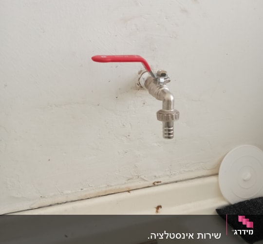 ברז עם ידית אדומה על קיר לבן